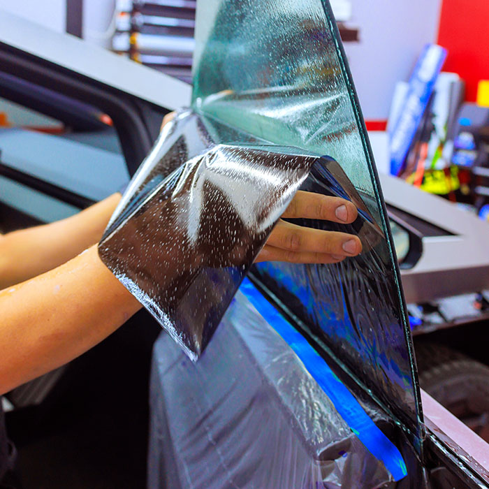 Worker technician applies window tint film to vehicle in workshop setting